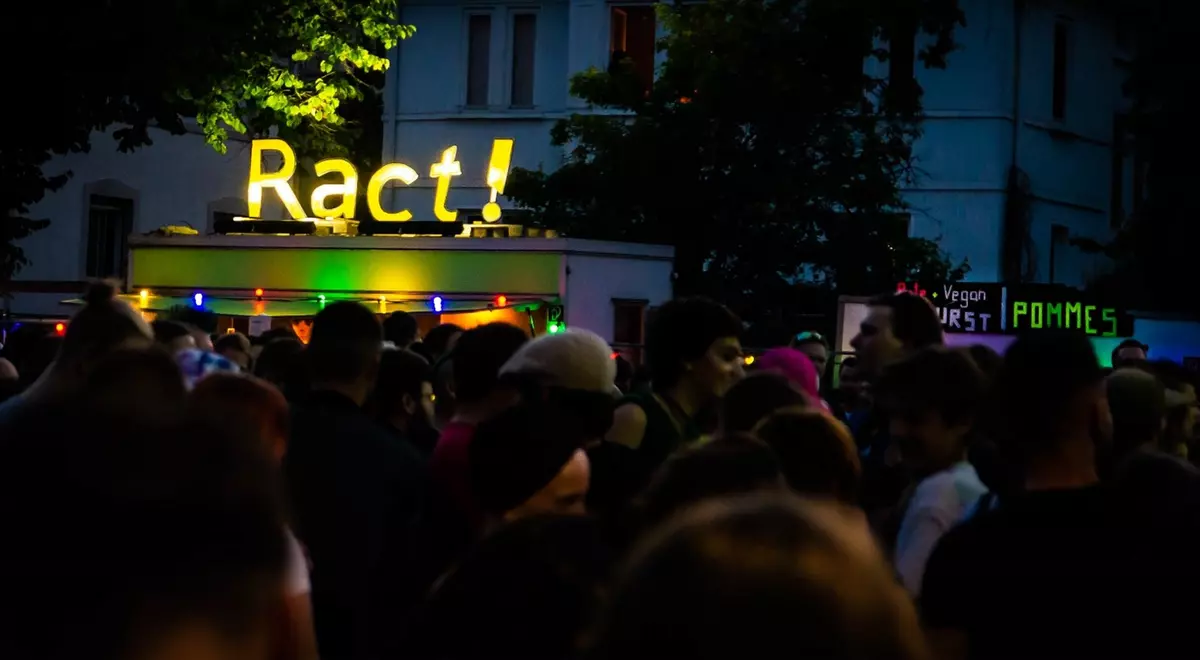 Titelbild Ract Infostand. Ract Schriftzug als gelbes Neonschild. Quelle: https//ract-festivals.de/medien/fotos/2022/
