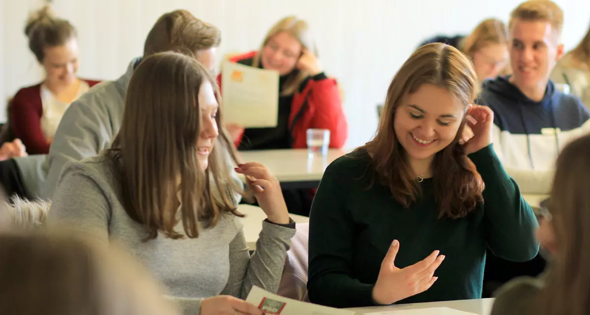 Schüler und Schülerinnen sitzen an Tischen und diskutieren